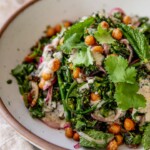 Side view of a bowl filled with broccolini date salad topped with sumac yogurt dressing, marinated onions and roasted chickpeas.
