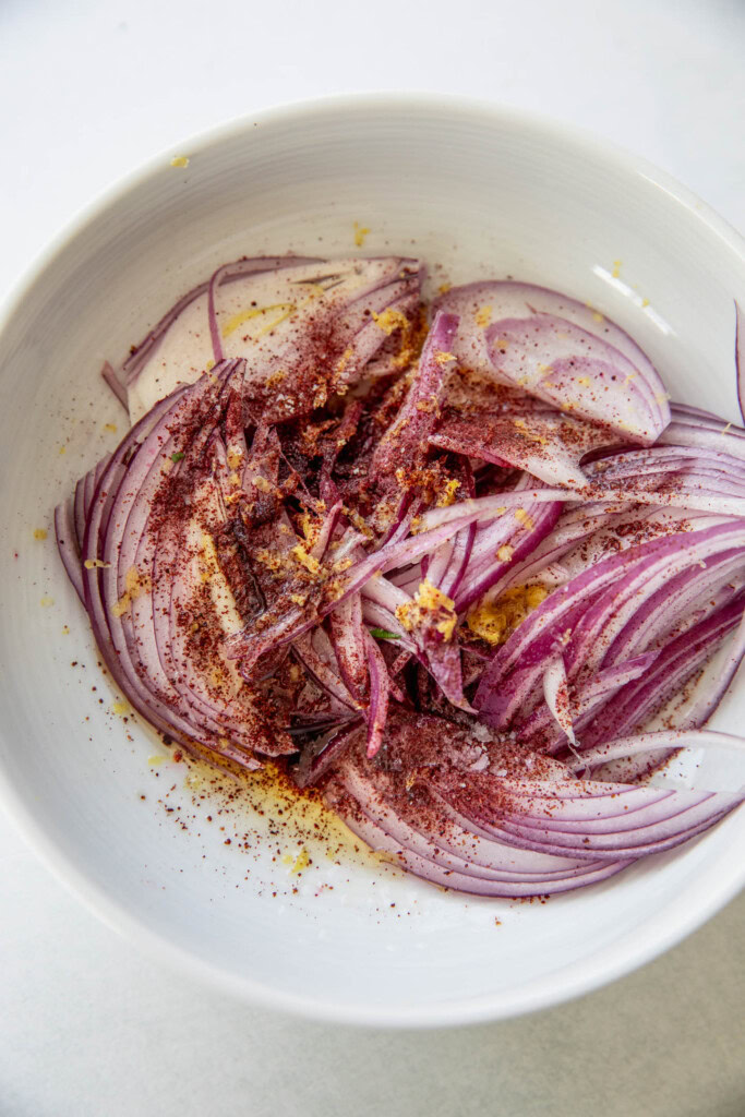 Bowl filled with red onions, lemon, sumac, oil, and maple syrup.