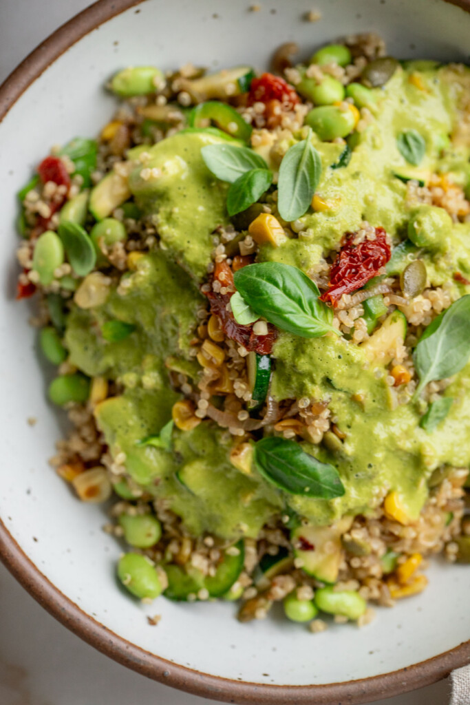Corn quinoa salad topped with a creamy basil dressing and fresh basil leaves.