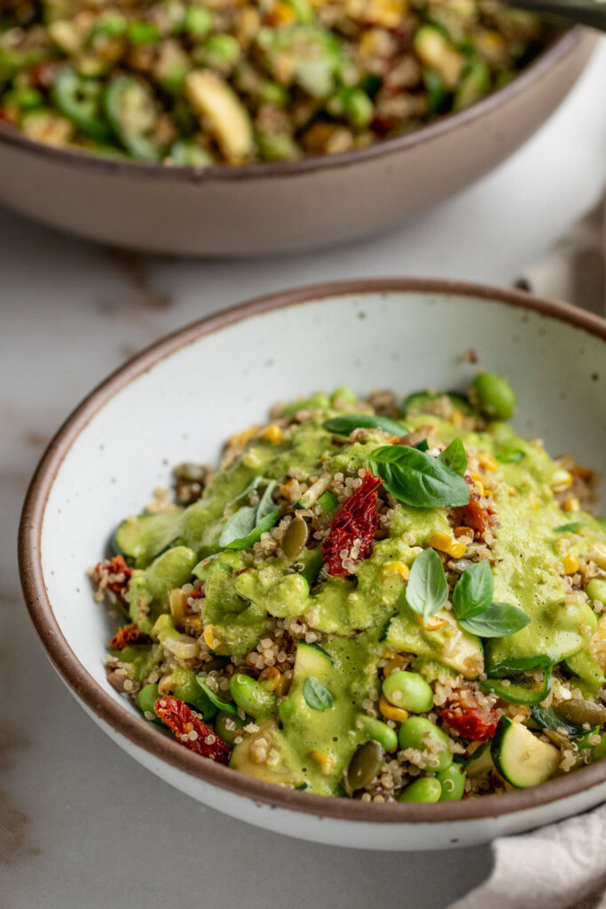 Side view of the quinoa salad dressed with creamy basil dressing next to the serving bowl of the quinoa salad.
