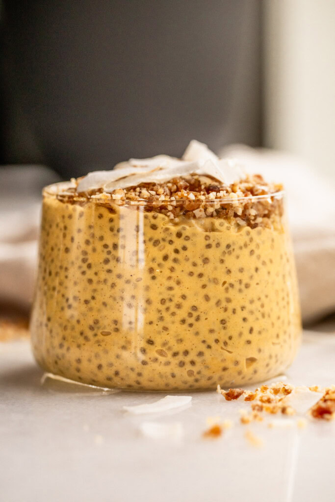 Full view of a cup of chia pudding topped with a crumble and coconut flakes.