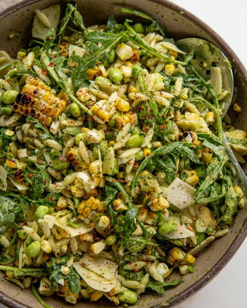 Mixing the corn orzo salad with scallion dill dressing in a bowl with a spoon.