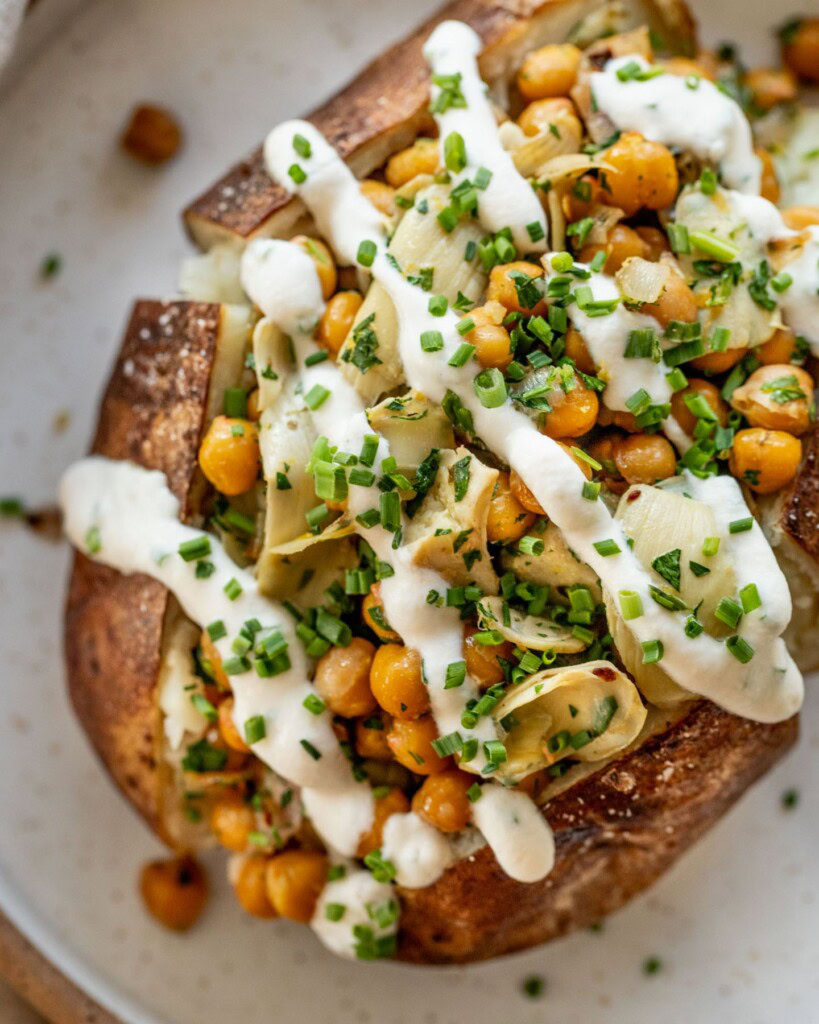 Close up of a chickpea artichoke stuffed baked potato drizzled with yogurt almond sauce. 