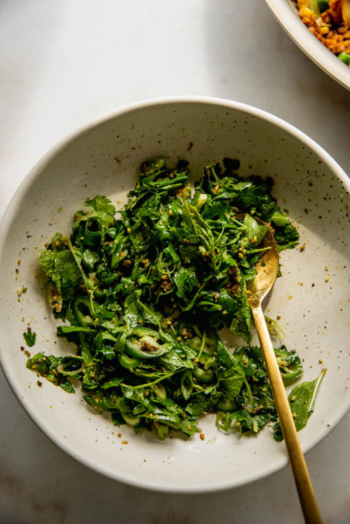 Mixed scallion and cilantro salad in a bowl with a gold spoon.