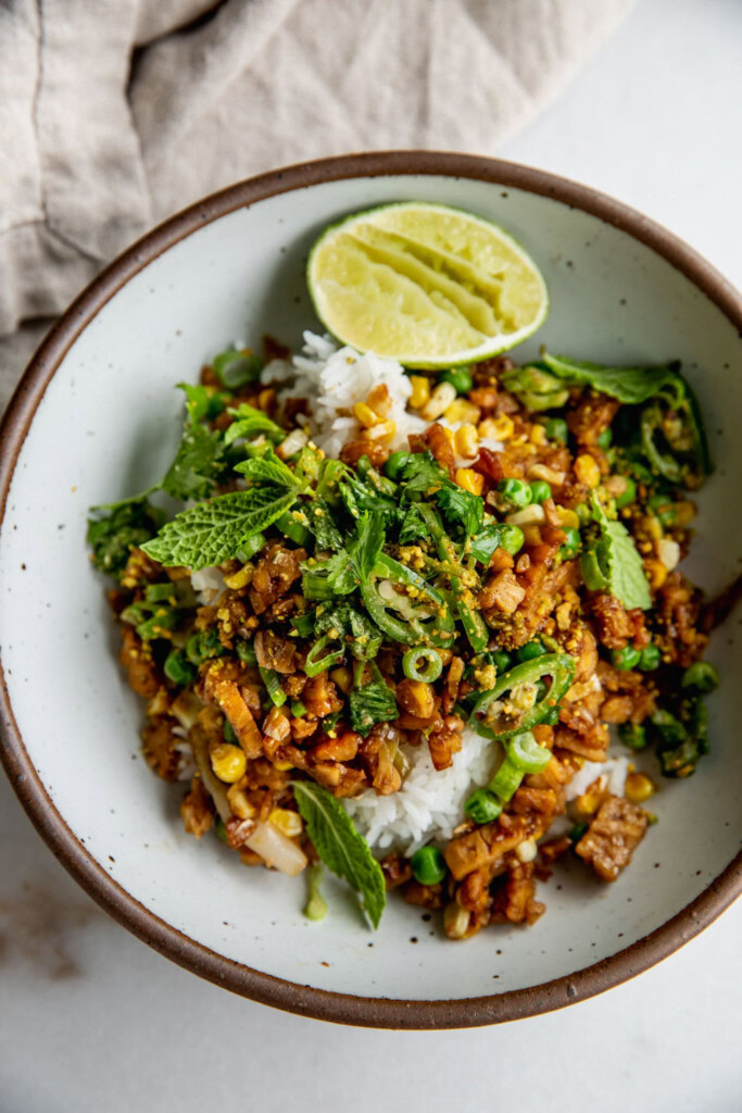 Top down view of a bowl of sticky tempeh piled on top of Jasmine rice and served with the scallion salad on top.