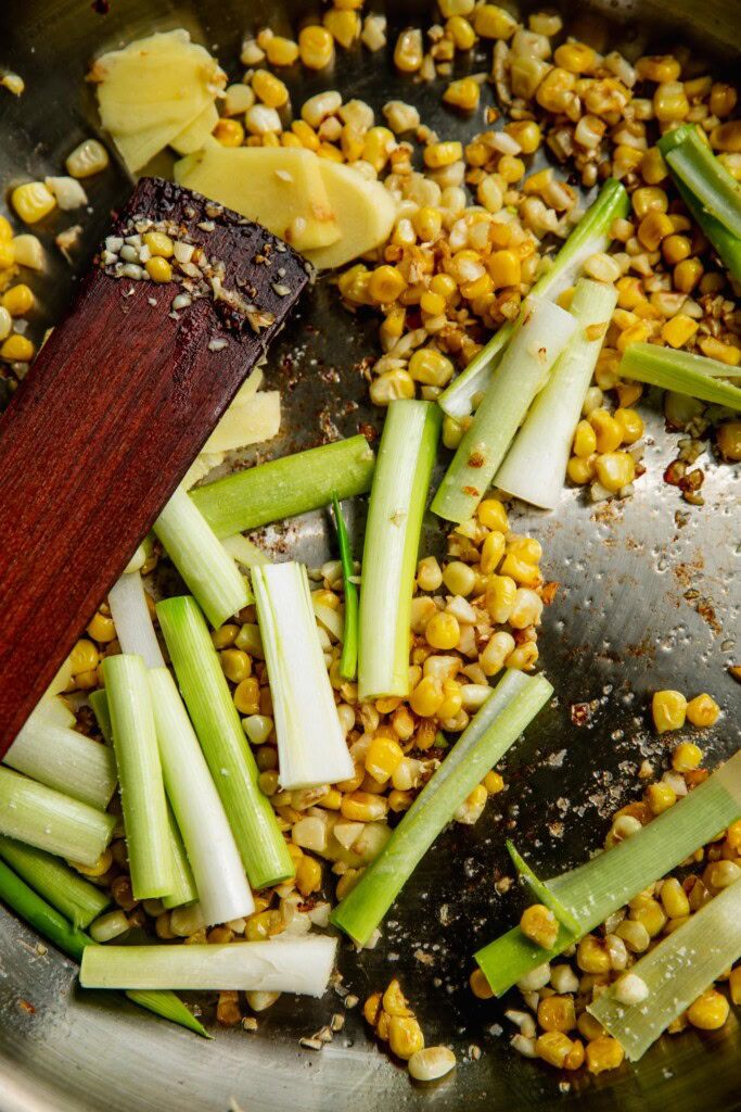 Sauteing the ginger, scallions, and garlic in with the charred corn in a pan.