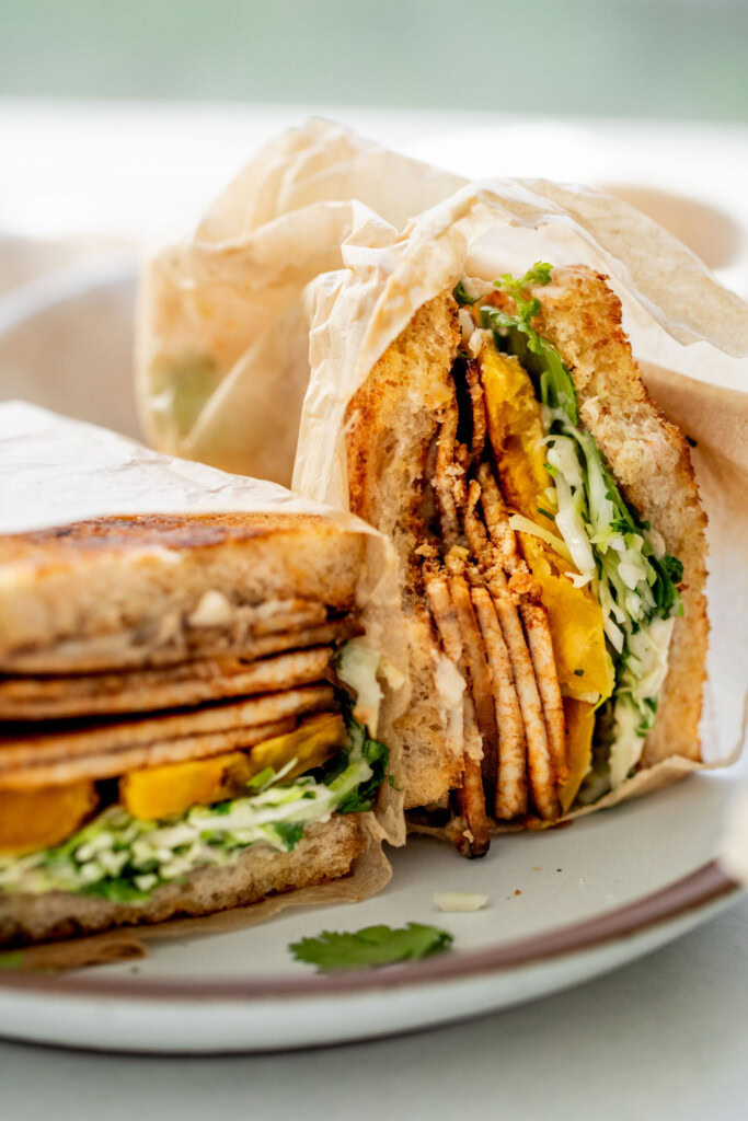 A halved tofu sandwich with layers of tofu deli slices, sweet plantain, and cabbage slaw.