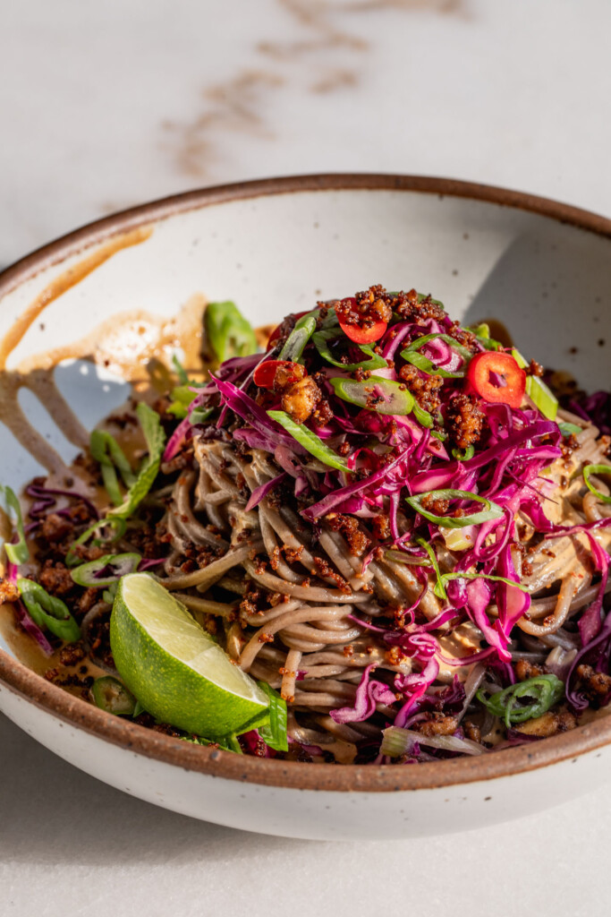 Bowl drizzled with sesame chili dressing and layered with noodles, cabbage slaw, and crumbled tofu.