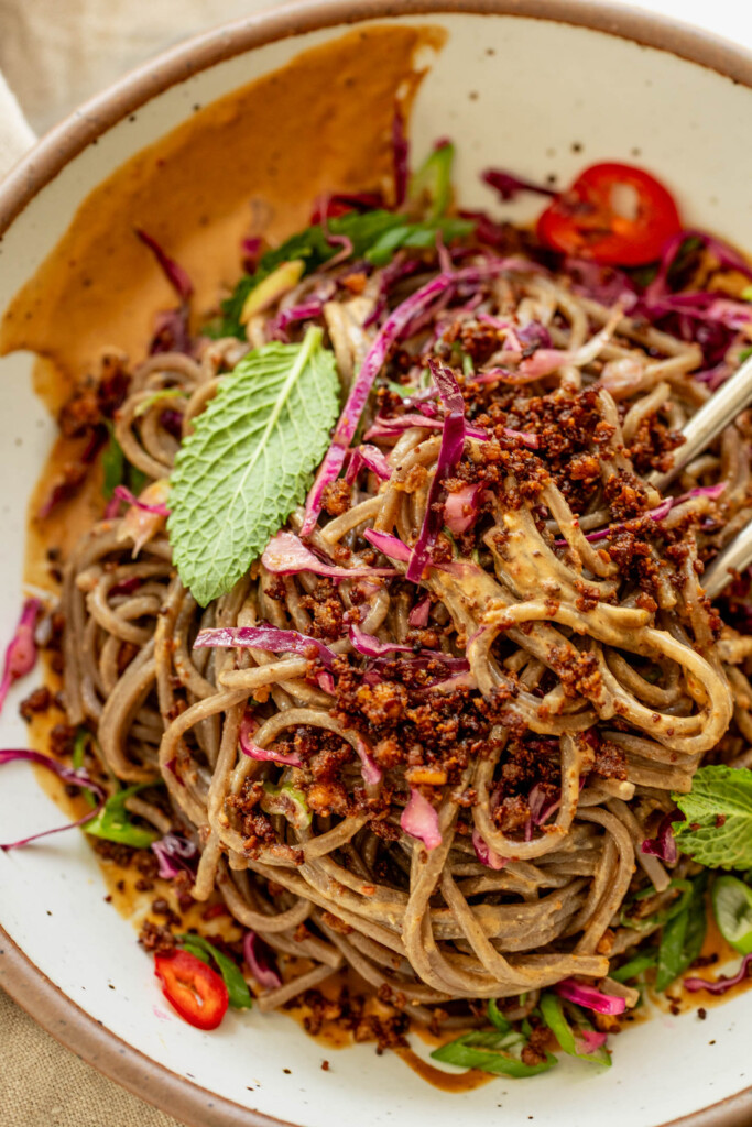 Mixing the noodles together with the sesame sauce and cabbage in a bowl with chopsticks.