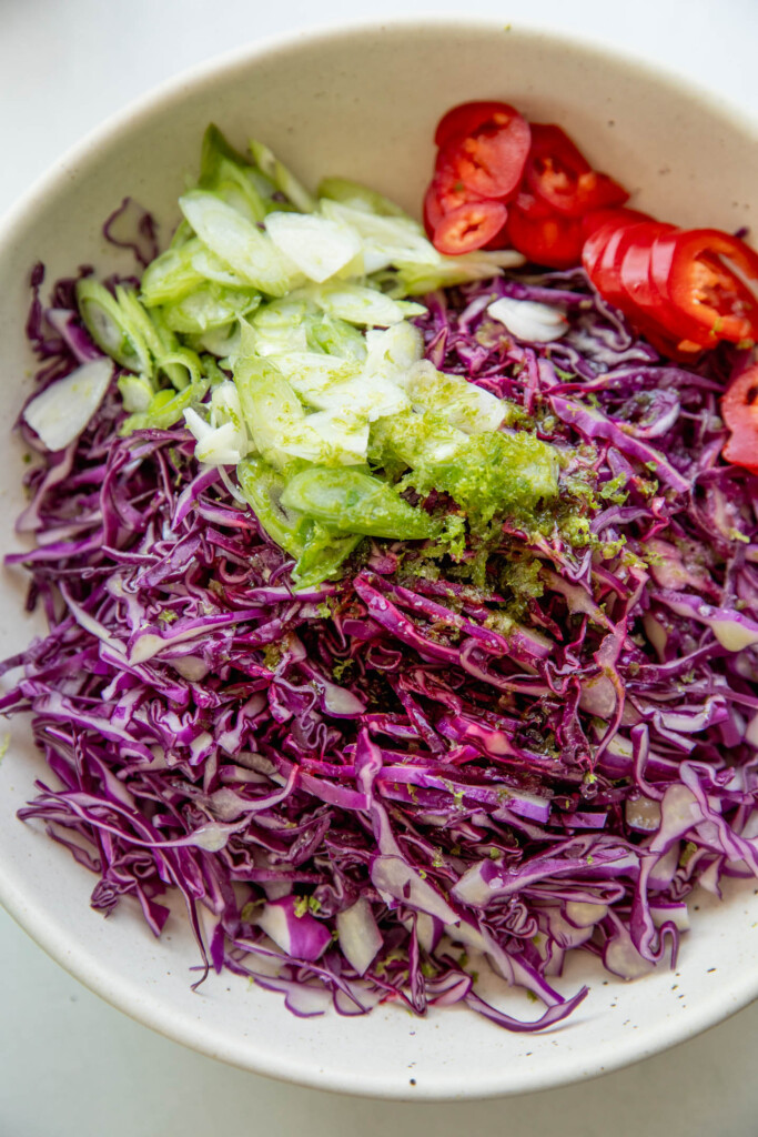 Bowl of shredded cabbage, chili pepper, and scallions in a mixing bowl.