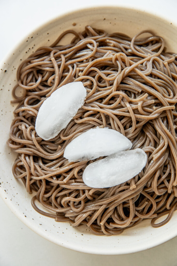 Cooked soba noodles in a bowl with ice cubes.