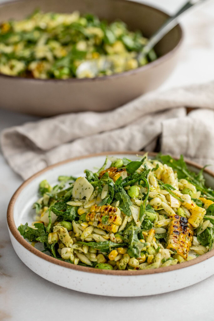 Plate of grilled corn orzo placed next to the mixing bowl of the salad.