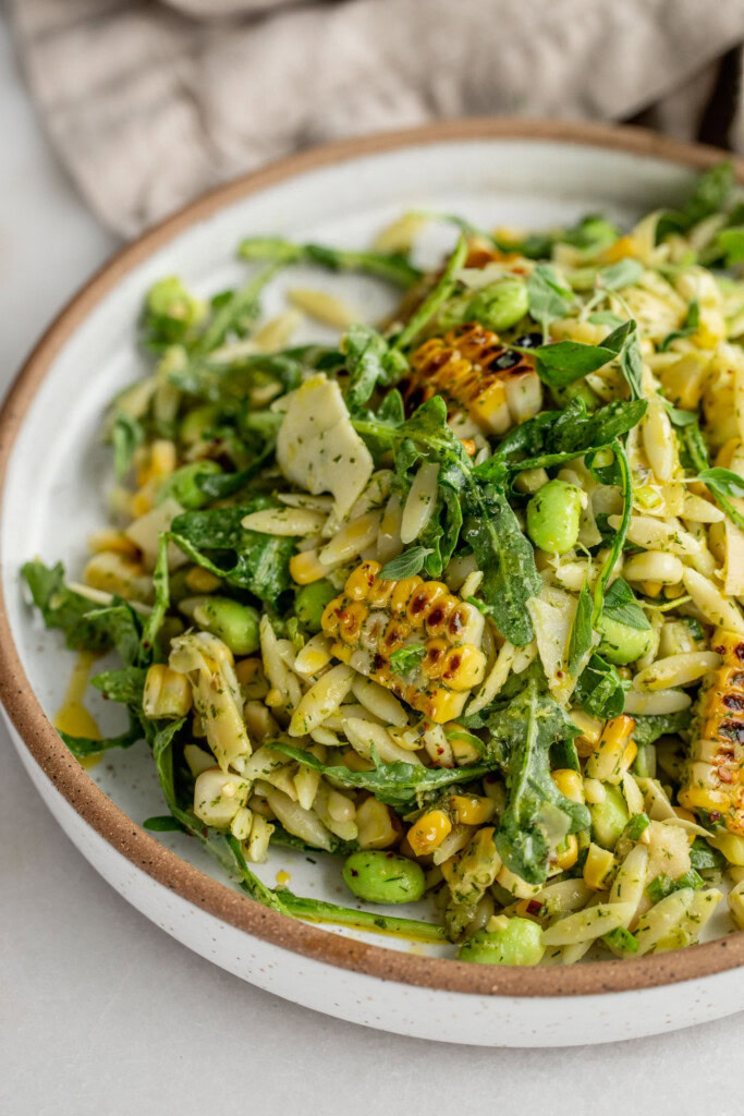 Side view of a serving plate of grilled corn and orzo salad mixed with vegan parm.