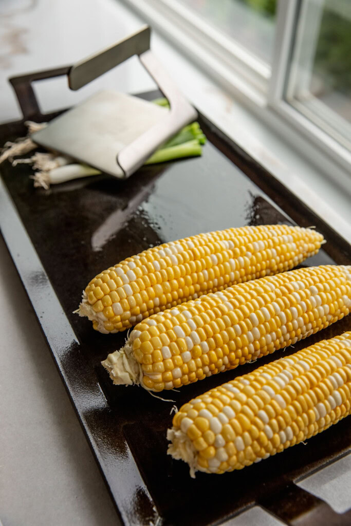 Corn on the cob and scallions being grilled on a cook top.
