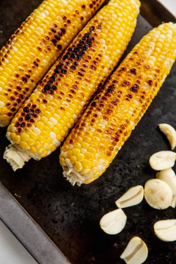 Grilled corn and cooked garlic on a grill pan.