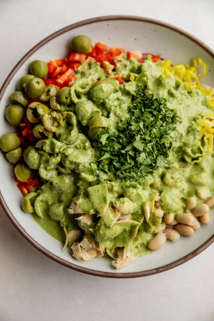 Bean salad of beans, bell pepper, olives, and artichoke hearts topped with the chive basil dressing and extra herbs on top.