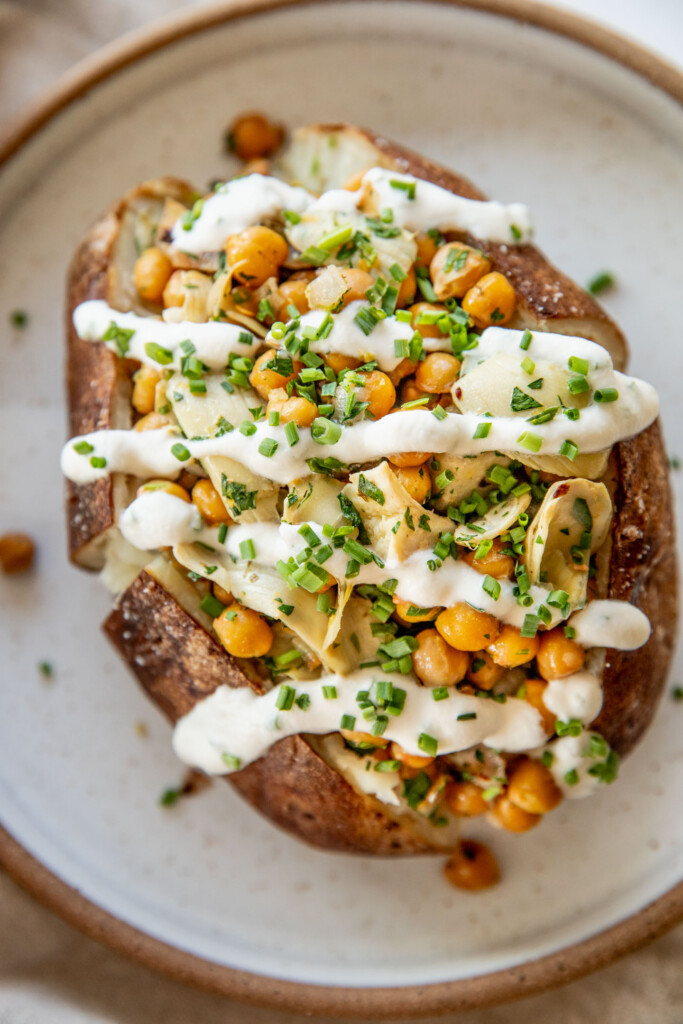 A jacket potato stuffed with a chickpea artichoke filling and drizzled with sauce.
