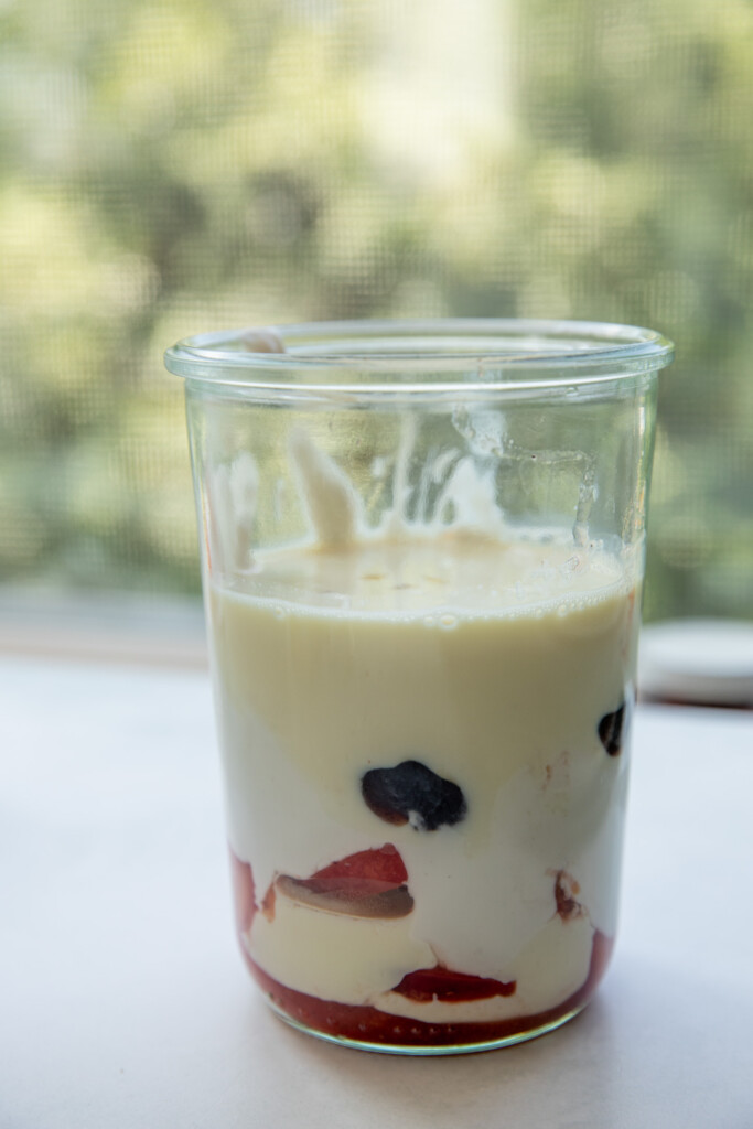 Blender cup filled with cooked peaches, yogurt, and milk.