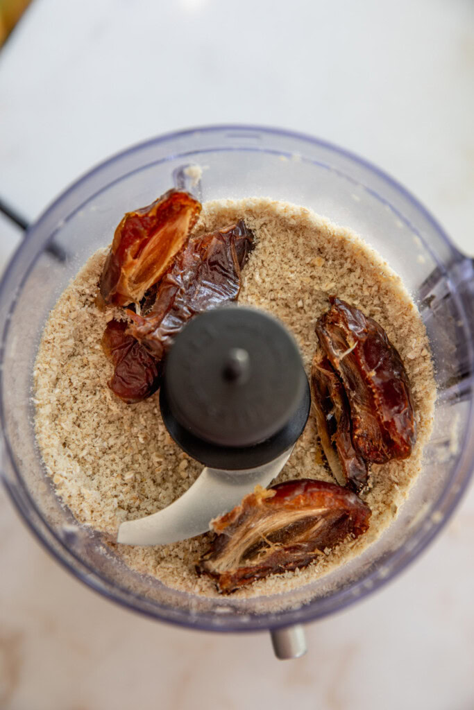 Adding the dates, almond flour, oats, and vanilla to a food processor.