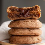 Stack of cookies on a plate with a cookie split in half is situated on top to show off the melted chocolate center.