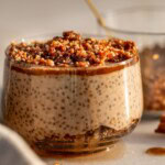 Close up of a cup of gingerbread cheesecake chia pudding layered with a gingerbread crumble with a cup of the extra crumble tucked behind the cup.