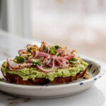 Toast on a plate topped with blended cilantro lime edamame and a pickled radish onion salad.