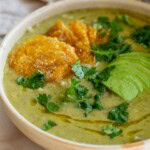 Bowl of salsa white bean soup topped with a drizzle of oil, crispy tostones, avocado slices, and cilantro leaves.