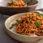 Bowl of rice topped with marinated carrot salad and crispy chickpeas with a mixing bowl filled with the carrot salad placed behind in the background.
