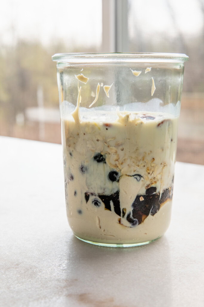 Blender cup filled with yogurt, blueberries, lemon, milk, oats, and pecans.