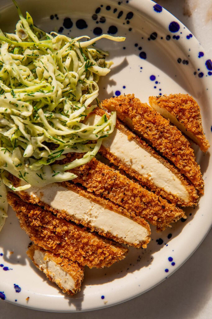 Close up of a cutlet cut into strips on a plate with cabbage slaw on the side.