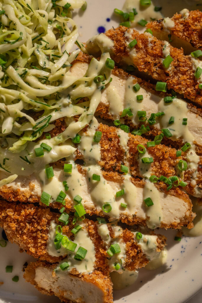 Close up of a cutlet cut up into strips and drizzled with the yogurt dressing.