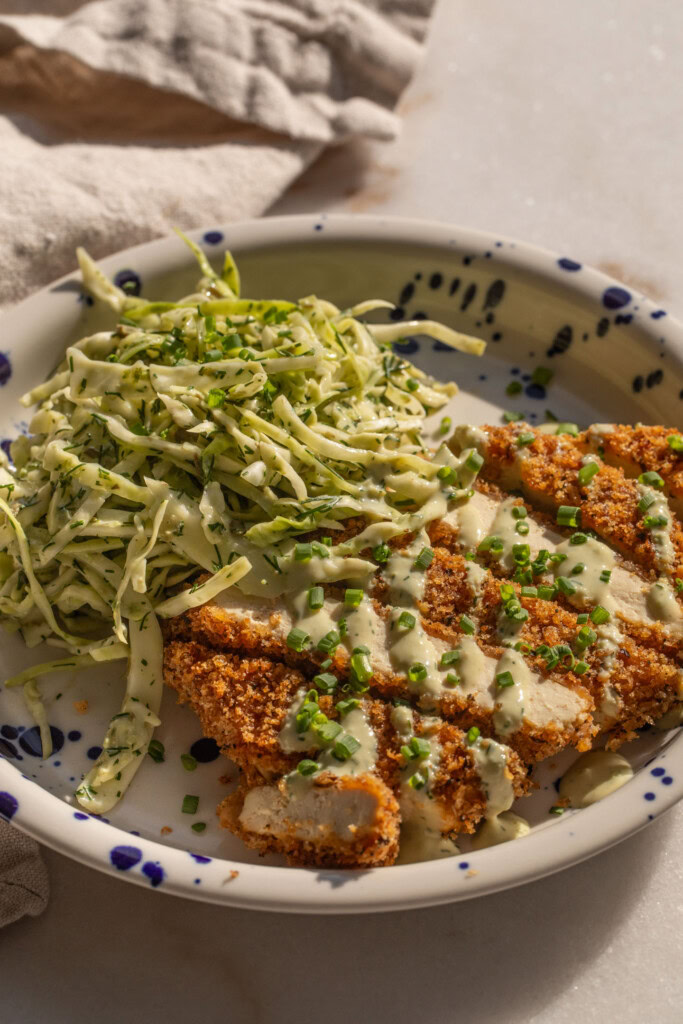 Side view of a plate of tofu cutlet cut into strips and served with slaw.