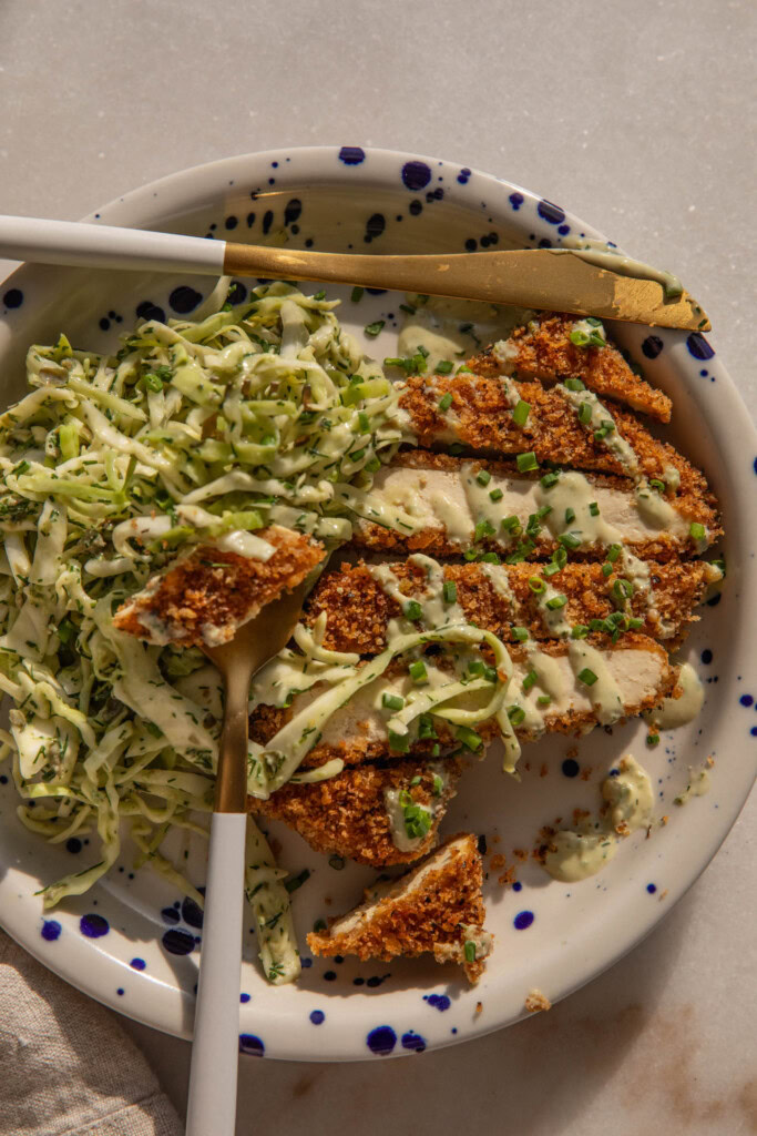 Plate of tofu cutlets being cut up with a fork and knife with a side of slaw.