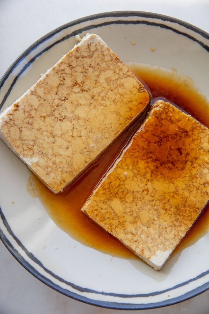 Tofu slabs in a plate being marinated with soy sauce and lemon.
