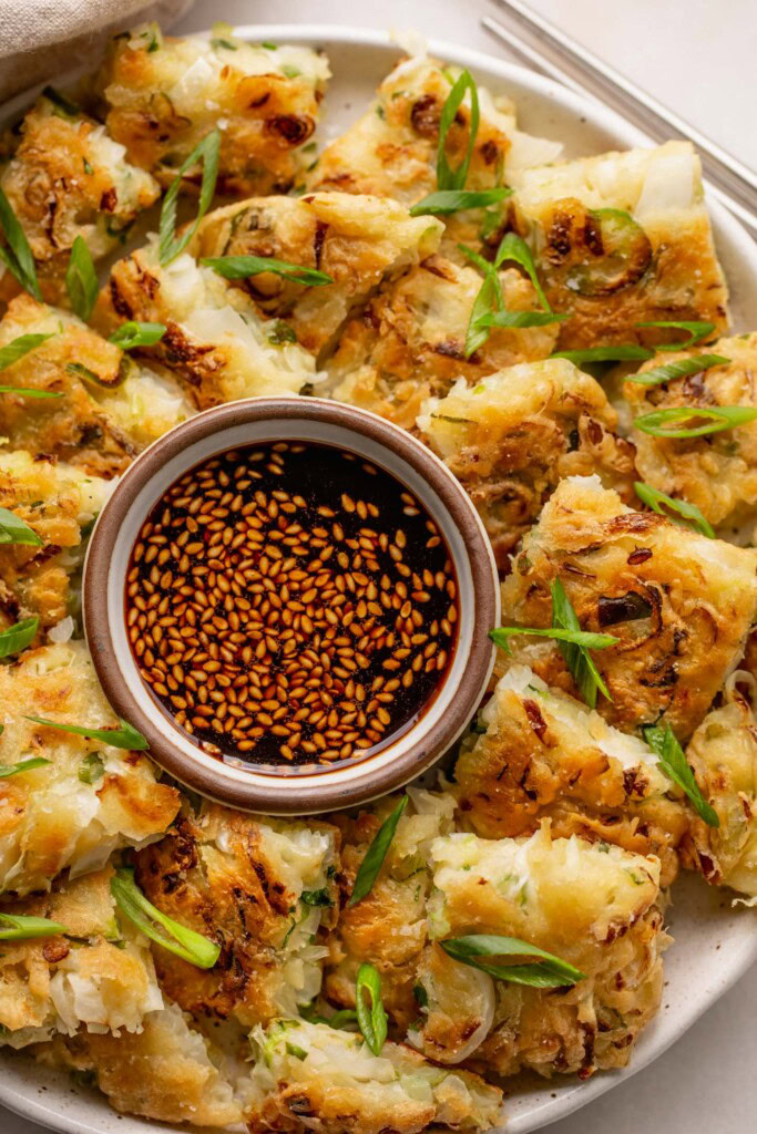 Close up of a plate of vegetable pancakes cut up and arranged around a bowl of dip.