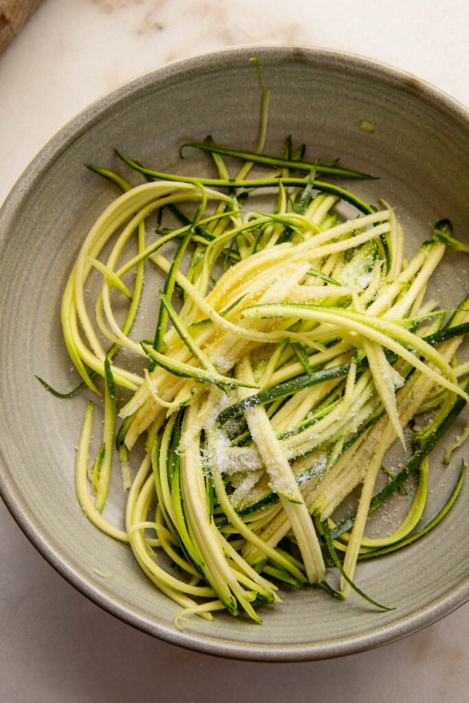 Shredded zucchini in a bowl with salt.
