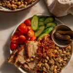 A plate assorted with torn pieces of bread, cherry tomatoes, cucumbers, gherkins, and marinated bean salad.