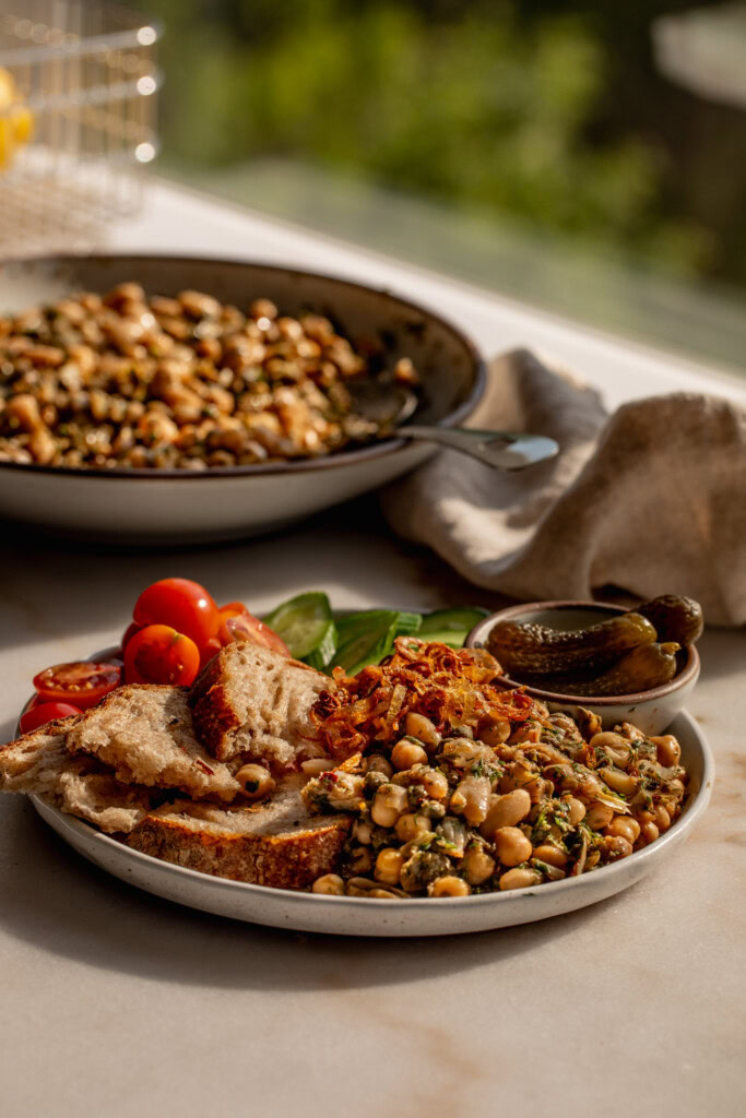 Side view of a plate filled with bean salad, bread, cherry tomatoes, and gherkins.