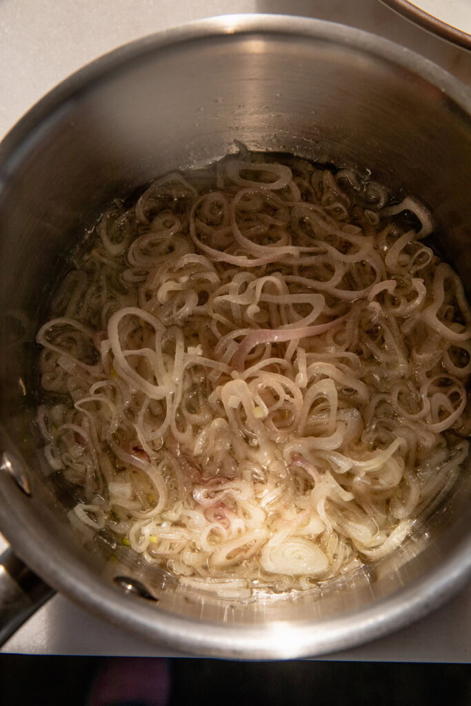 Shallot slices cooking in oil in a saucepan.