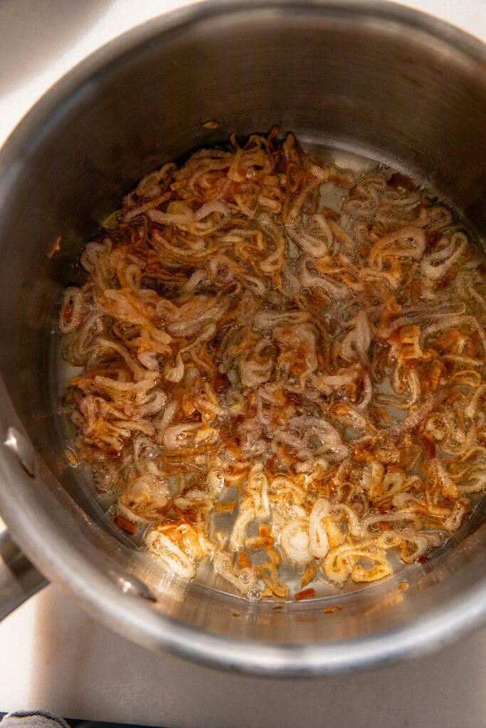 Golden crispy shallots cooking in oil in a saucepan.