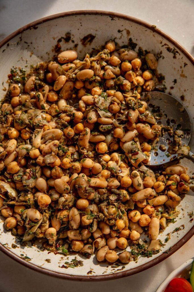 Beans being tossed together with artichoke hearts, herbs, balsamic vinegar, shallot oil, garlic, and lots of lemon.