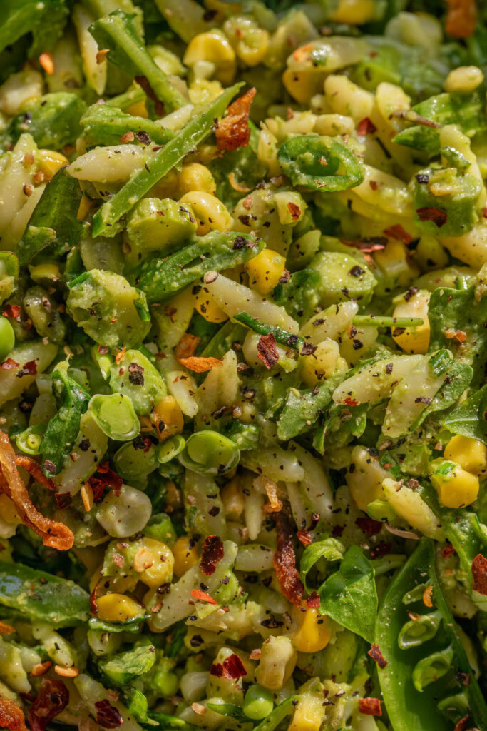 Close up of a bowl of pasta salad tossed with orzo, corn, asparagus, and snap peas.