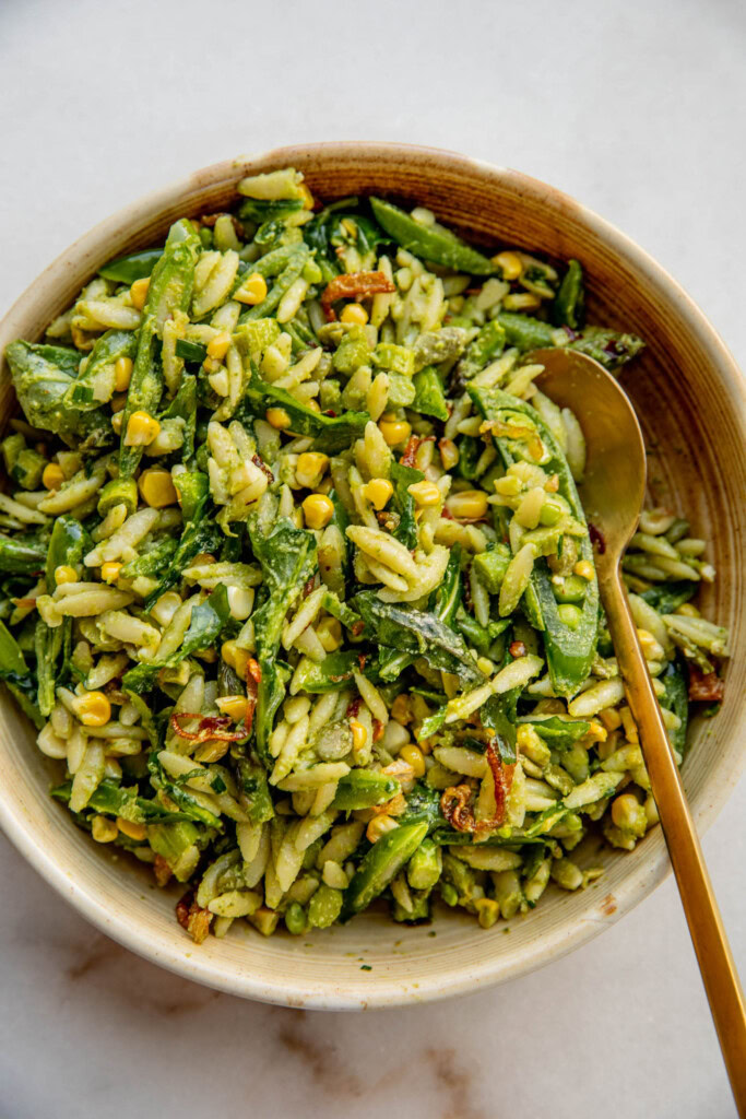 Digging into a bowl of pasta salad with a gold spoon.