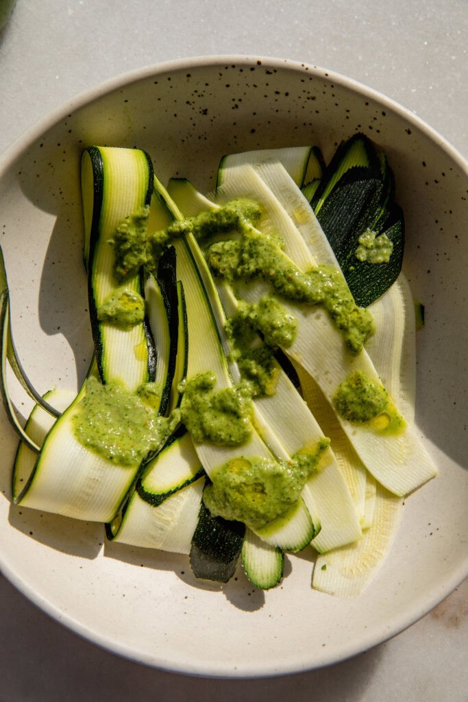 Adding some zhug on top of the zucchini ribbons in a bowl.