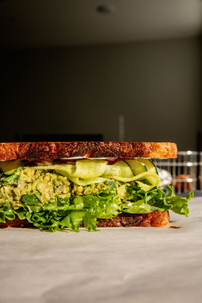 Sandwich stuffed with green chickpea salad, lettuce, zucchini ribbons, and pickled shallots.