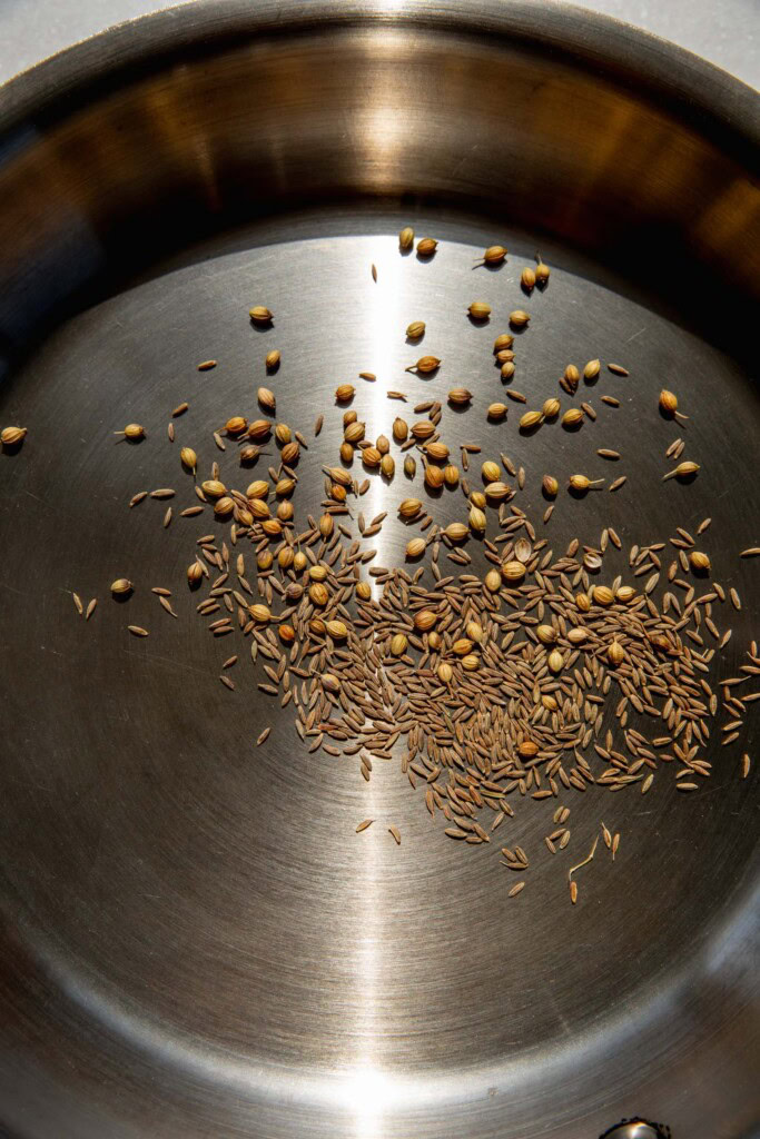 Toasting cumin and coriander seeds in a pan.