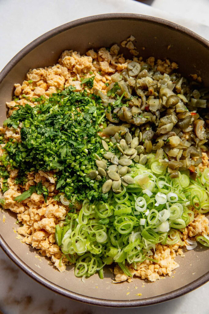 Bowl filled with mashed chickpeas, scallions, cilantro, pepitas, and pickled jalapeños.