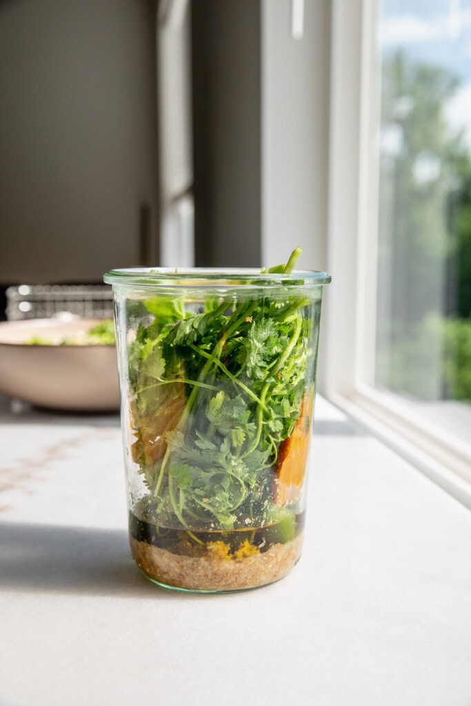 Blender cup filled with mashed spices and garlic, oil, cilantro, lemon juice, and mustard.
