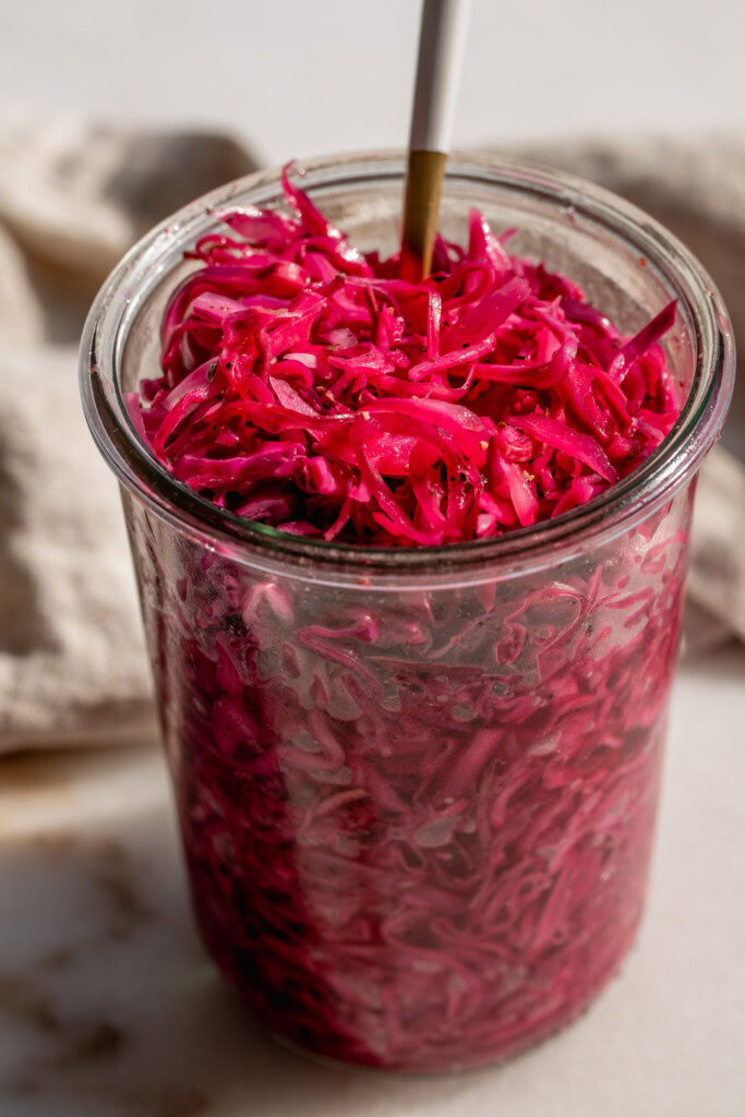Picking up pink slaw from the top of the storage container with a fork.