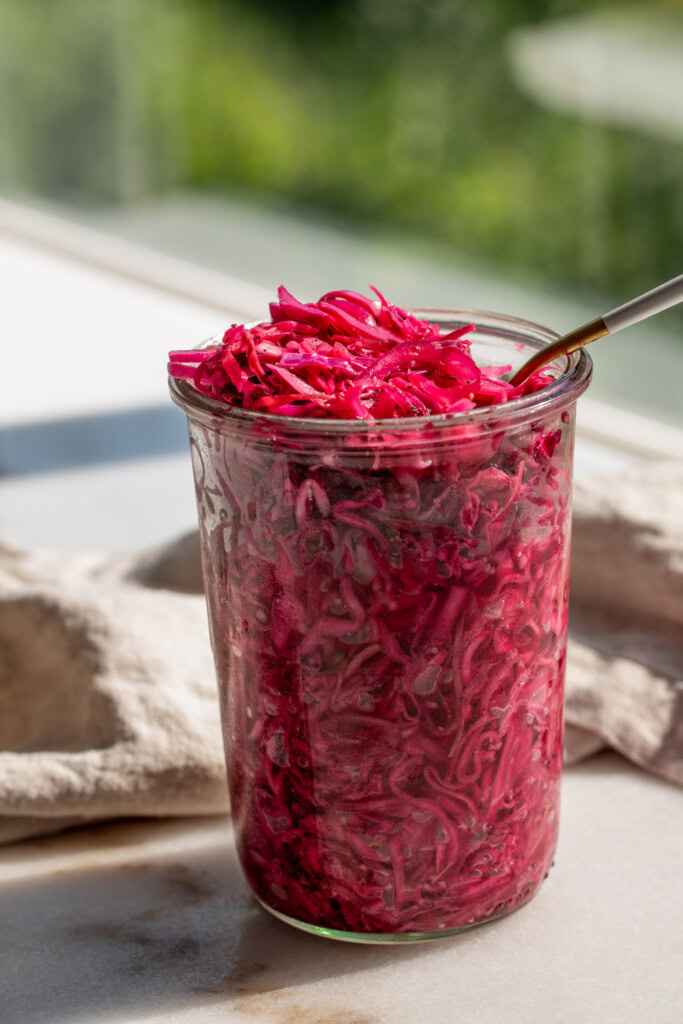 Close up of a jar of red cabbage slaw being mixed with a fork.